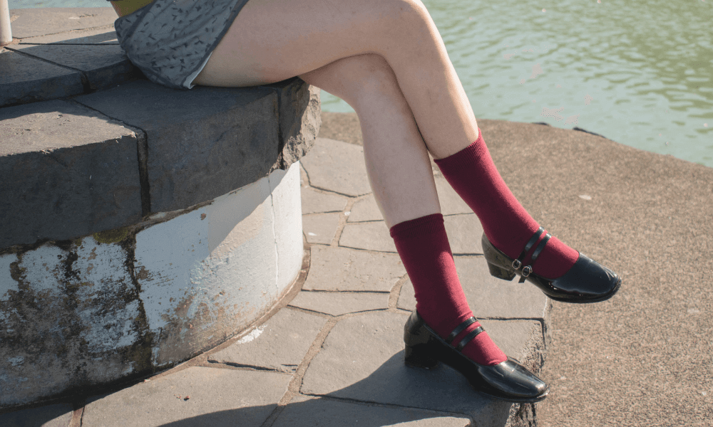 Young woman wearing burgundy socks and stylish shoes, sitting by water.